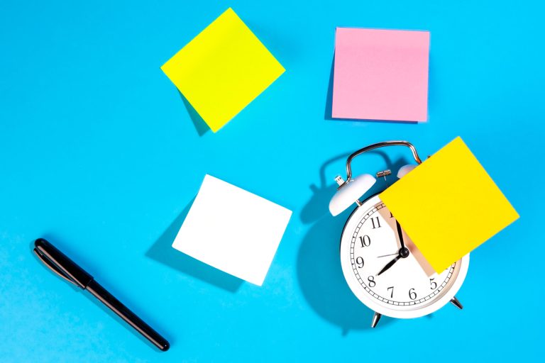 Alarm clock and colorful blank paper reminders on a blue background, top view. Notes with empty place for text.
